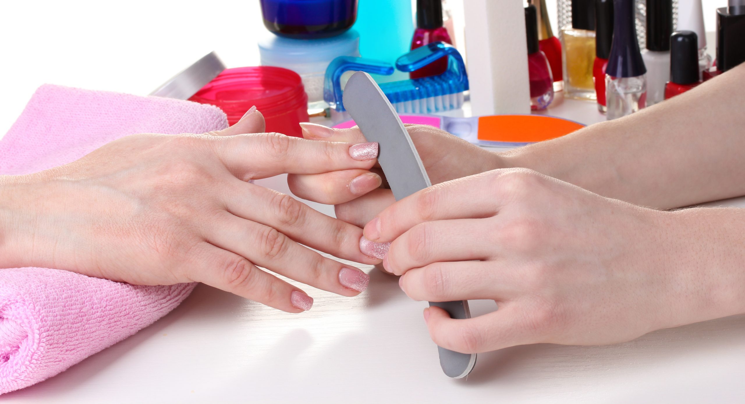 Nail technician filing client’s nails with emery board during professional manicure session