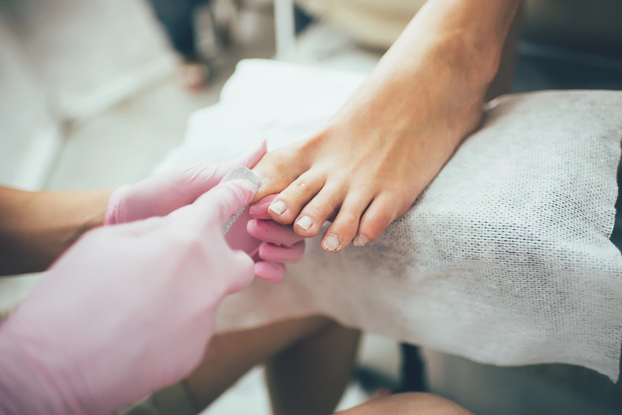 Pedicure in progress with a technician filing toenails wearing pink gloves in a salon setting