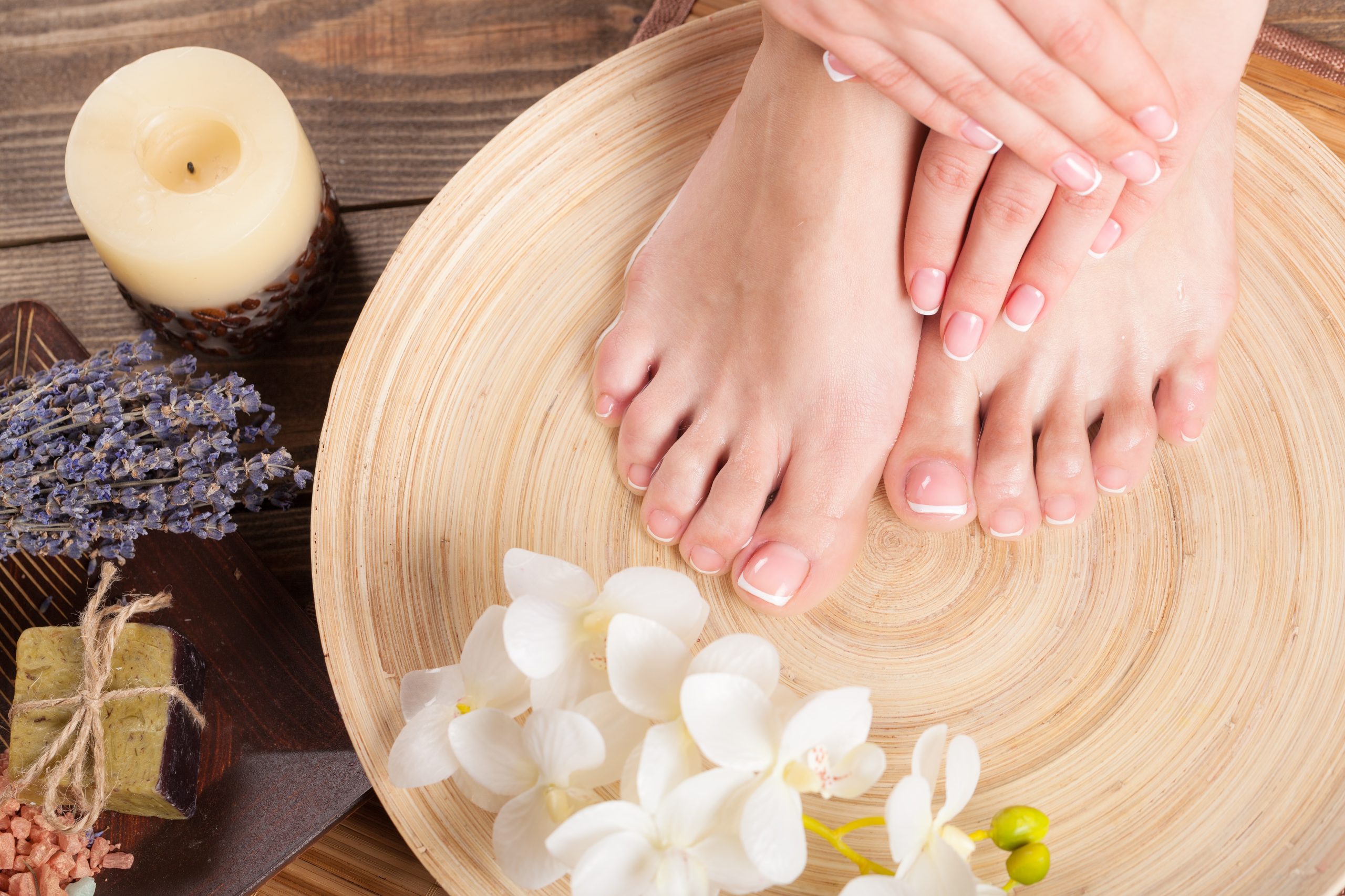 Manicured hands and feet with French nails in a spa setting with flowers, lavender, and candle