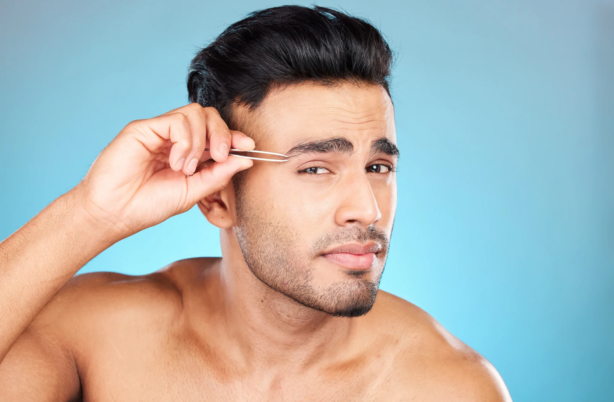 Close-up of tweezing unwanted eyebrow hairs from below the brow for a sharper look.