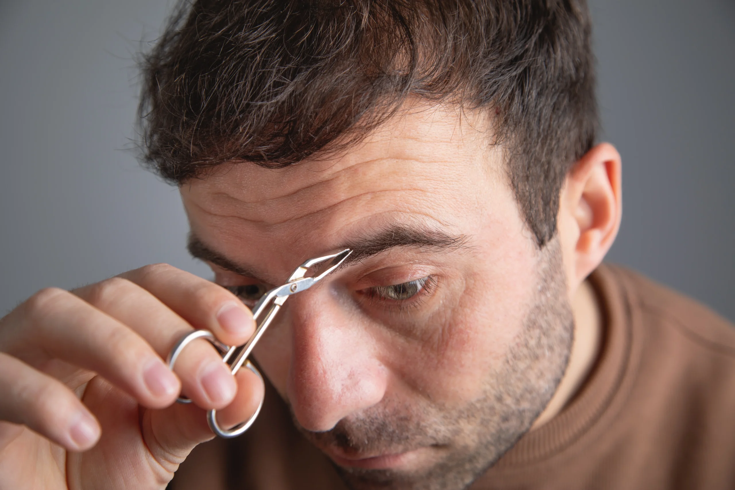 Set of essential eyebrow grooming tools for men including tweezers, scissors, spooled, and electric trimmer.