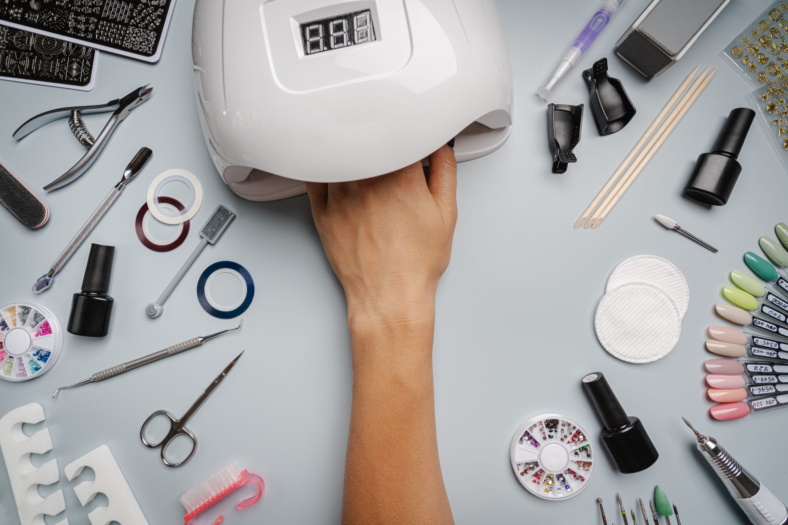 Hand in UV nail lamp with manicure tools and gel polish on a table