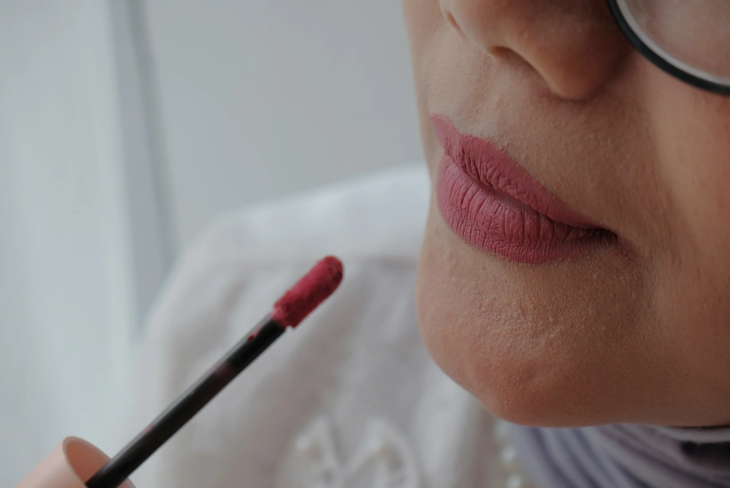 woman applying berry lipstick, close-up of glossy nude lipstick