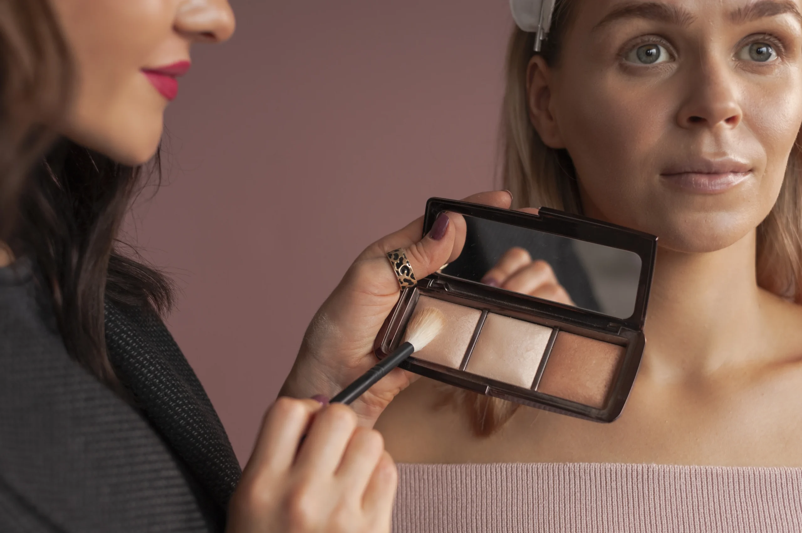 Makeup artist applying cream highlighter on cheekbones for radiant finish.